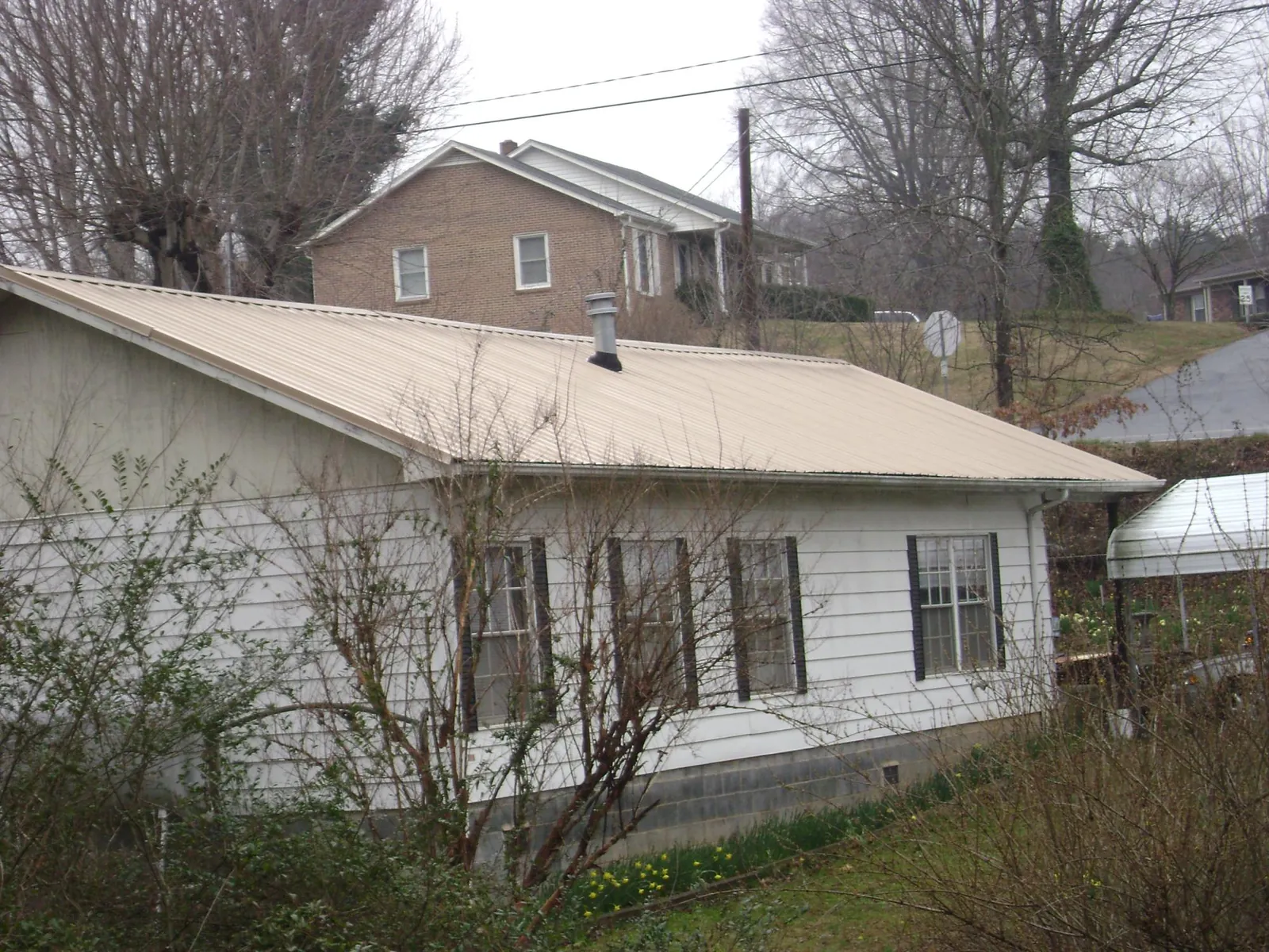 Tan metal roof on a white sided house set into a hillside — Commercial Roofing by Roofing Brothers in Englewood